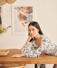 model wearing white floral smocked blouse leaning on table